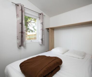 Chambre double lumineuse avec lit couverture et fenêtre au Camping La Belle Etoile