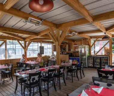 Salle de restauration en bois avec tables et chaises au Camping La Chênaie