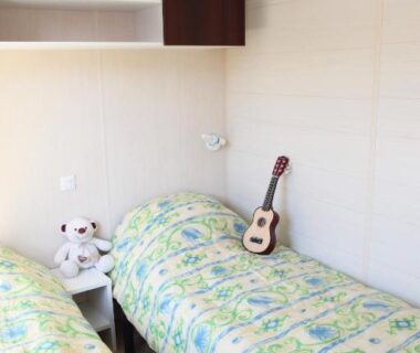 Dans la chambre avec deux lits simples et un ukulélé au Camping La Clé des Champs