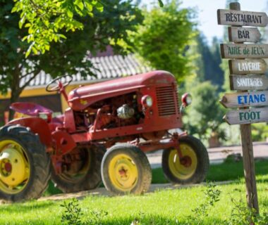 Allée herbeuse avec tracteur ancien et panneau directionnel au Camping La Ferme de Perdigat