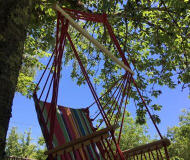 Pelouse et fauteuil suspendu sous un arbre au Camping La Ferme de Perdigat