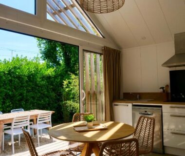 Séjour ouvert avec table ronde et chaises en osier sur terrasse au Camping La Forêt