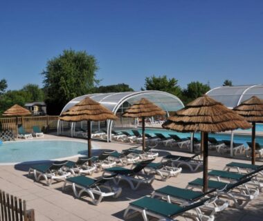 Piscine extérieure avec transats et parasols en paille au Camping La Mignardière