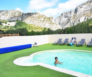 Piscine extérieure avec transats devant les falaises au Camping La Pinatelle