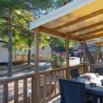 Terrasse couverte avec table et chaises au milieu des pins au Camping La Pinède