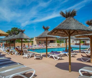 Bord de piscine avec parasols et transats au Camping La Pinède
