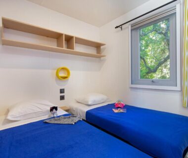 Chambre avec deux lits et fenêtre sur arbres au Camping La Pinède
