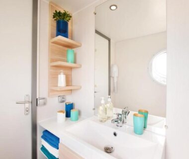 Salle de bains avec lavabo miroir étagères et hublot du Camping La Plage