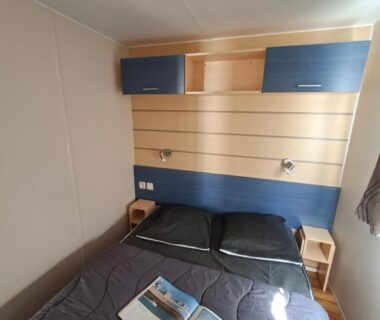 Chambre avec lit double, rangements et lampes liseuses dans le camping La Prévoté