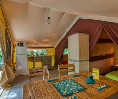 Intérieur de tente aménagée avec coin repas réfrigérateur et lit au Camping La Sagne