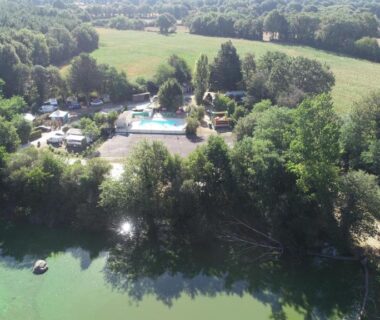 Bord du lac avec piscine et emplacements entourés d'arbres au Camping La Venise Du Bocage