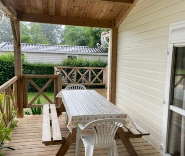 Terrasse couverte avec table en bois et chaises blanches du Camping La Venise Du Bocage