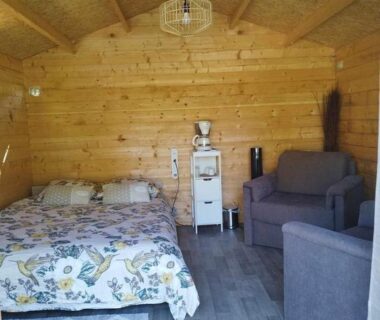 Intérieur de chalet en bois avec lit et fauteuil au Camping La sablière