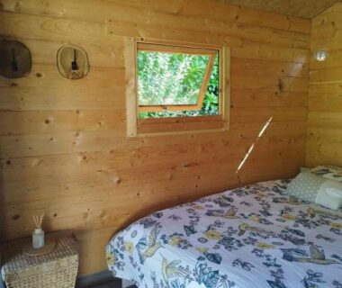 Intérieur de cabane en bois avec lit et petite fenêtre au Camping La sablière