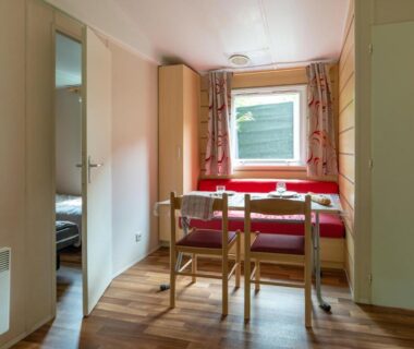 Coin repas près de la fenêtre avec table et banquette dans l'hébergement du Camping Le Barutel