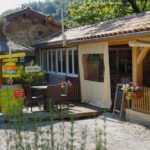 Terrasse extérieure avec tables, fleurs et panneaux directionnels au Camping Le Barutel