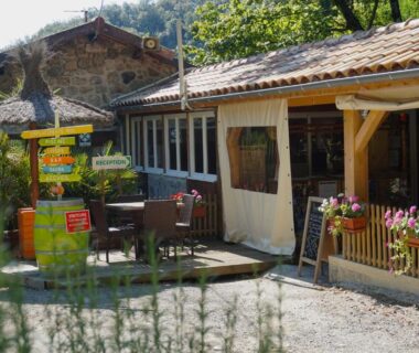 Terrasse extérieure avec tables, fleurs et panneaux directionnels au Camping Le Barutel