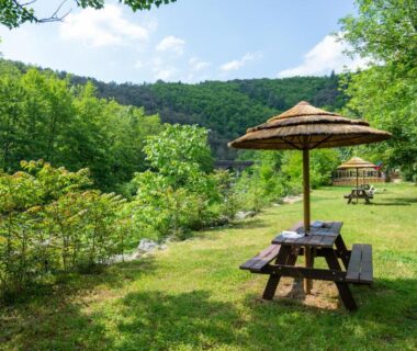 Bord de rivière avec tables et parasols au Camping Le Barutel