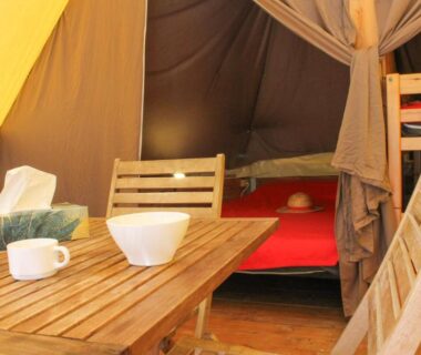 Intérieur de tente aménagée avec table en bois et lits au Camping Le Bois De Pins