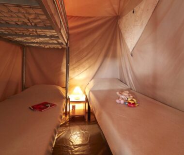 Intérieur de tente avec deux lits lampe et table de chevet au Camping Le Both d'Orouet