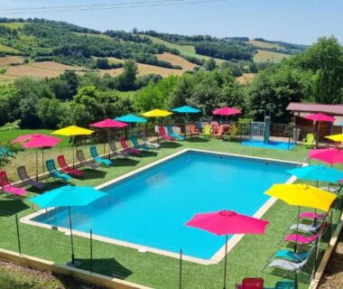 Piscine extérieure bordée de parasols et transats dans la campagne ariégeoise au Camping Le Bourdieu