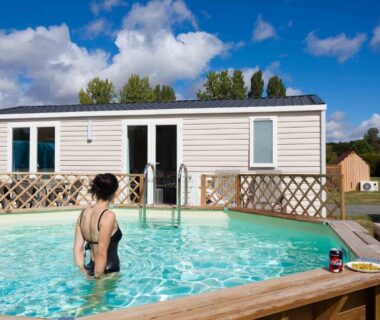 Piscine extérieure et mobil-home en arrière-plan au Camping Le Cardinal