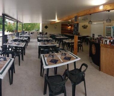 Terrasse couverte avec tables et vue sur la piscine du Camping Le Chassezac