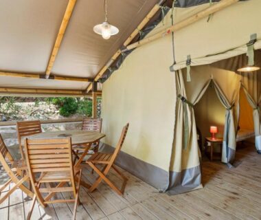 Terrasse en bois avec table et chaises à l'entrée d'une tente au Camping Le Damier