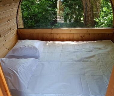 Intérieur cabine avec lit double et fenêtre ronde donnant sur la végétation au Camping Le Douzou