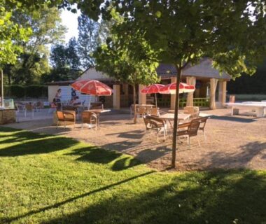 Terrasse ombragée avec tables et parasols au camping Le Douzou