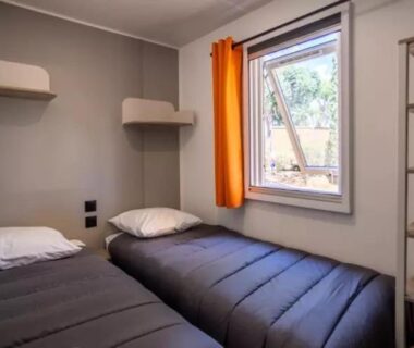Chambre avec deux lits simples et fenêtre dans le mobil-home Le Hameau des Pins
