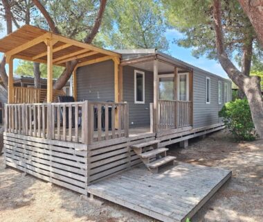 Mobil-home sur terrasse en bois ombragée sous pins au Camping Le Mas