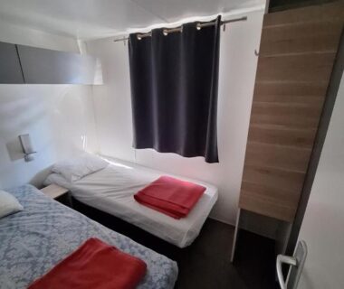 Chambre avec deux lits armoire et rideau dans le Camping Le Mas