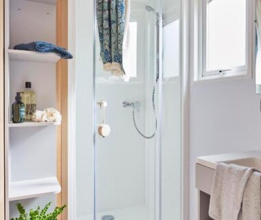 Salle de bain avec cabine de douche et étagères au Camping Le Mas de Reilhe