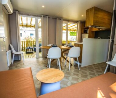 Intérieur séjour avec canapé table et kitchenette dans le mobil-home du Camping Le Paradis Carcans Lacanau