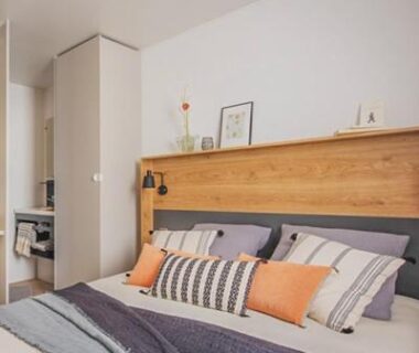 Chambre avec lit double tête de lit en bois et coussins au Camping Le Perpetuum