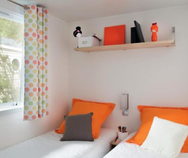 Chambre avec deux lits et coussins orange au Camping Le Perpetuum