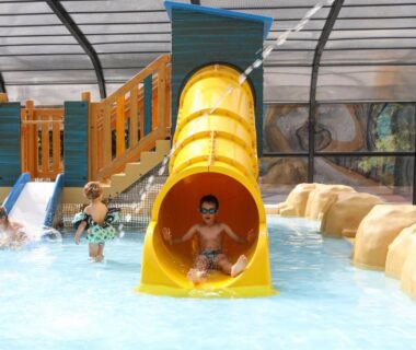 Piscine couverte avec toboggan jaune et enfants au Camping Le Petit Rocher