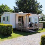 Mobil-home avec terrasse sur pelouse entouré de haies au Camping Le Picard