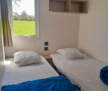 Intérieur chambre avec deux lits simples et fenêtre sur pelouse du Camping Le Picard