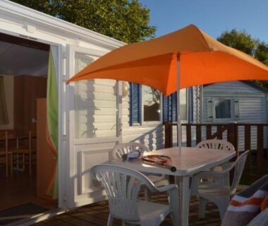 Terrasse avec parasol orange table et chaises au Camping Le Puits Rochais