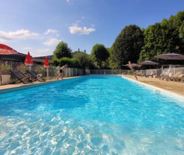 Piscine extérieure entourée de parasols et transats au Camping Le Soulhol