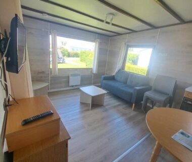 Salon intérieur avec canapé télévision et table dans le mobil-home du Camping Les 2 Plages
