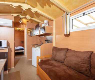 Intérieur de mobil home avec canapé et kitchenette au Camping Les Amandiers