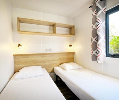 Chambre avec deux lits simples et fenêtre sur végétation dans le mobil-home du Camping Les Castors