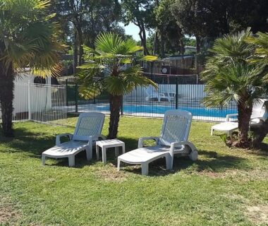 Pelouse avec transats et piscine clôturée au Camping Les Chênes Verts