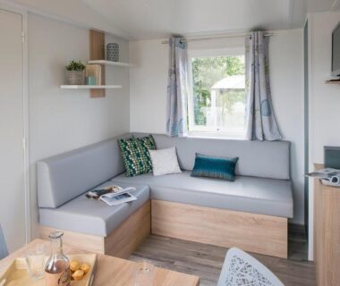 Intérieur de mobil‑home avec banquette, table et télévision au Camping Les Chênes Verts