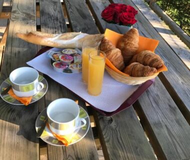 Table en bois avec croissants, jus d'orange et tasses au Camping Les Chèvrefeuilles