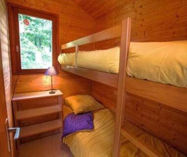 Cabine en bois avec lits superposés et fenêtre sur la nature au Camping Les Etoiles