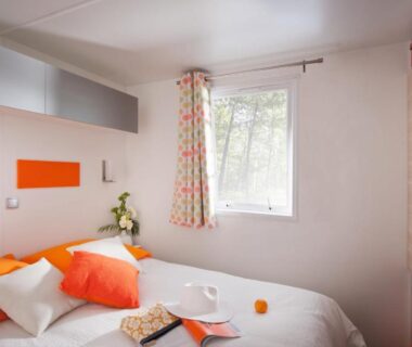 Chambre avec lit, coussins et rangements orange au Camping Les Jardins de la Mer